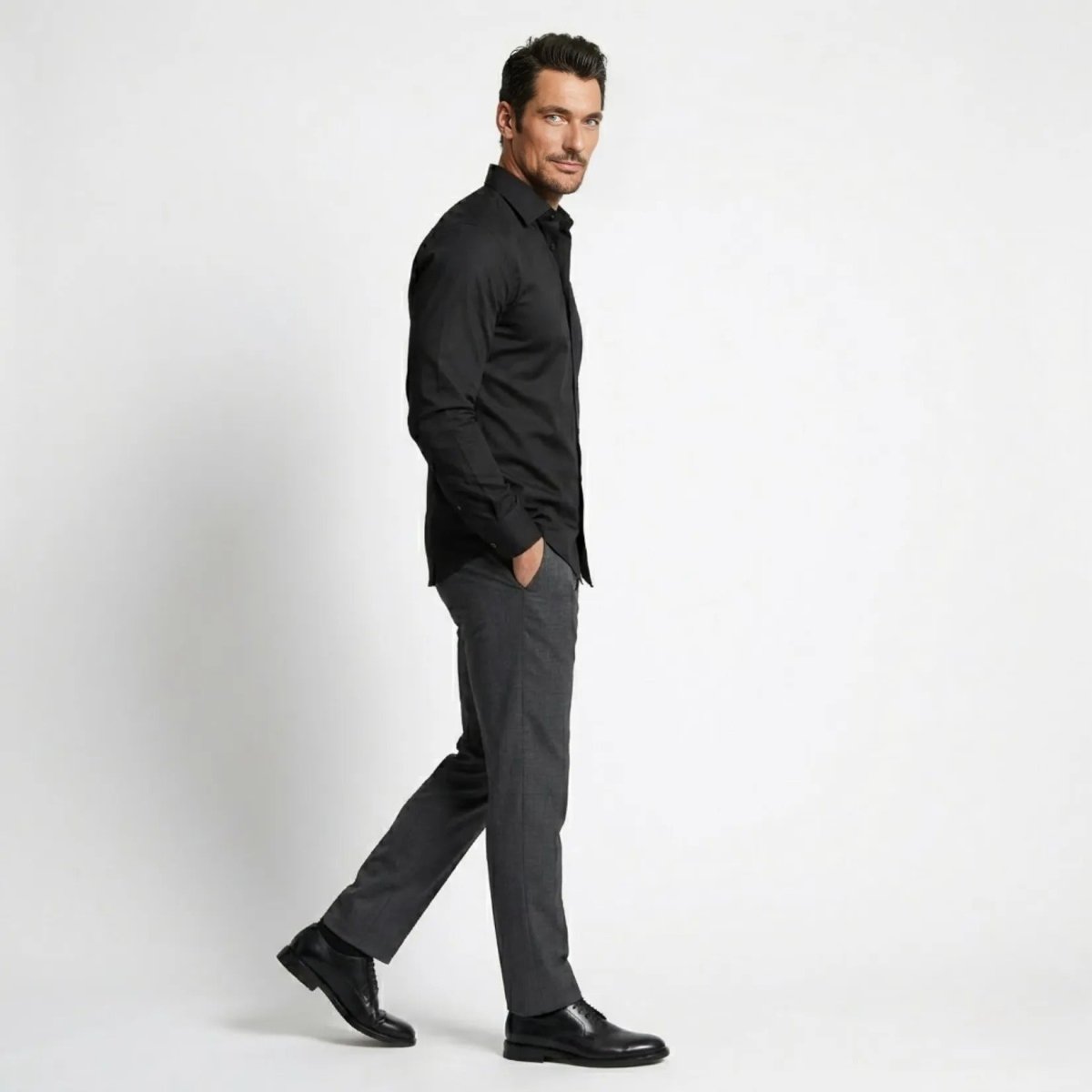 Side profile of male model walking in a luxury slim fit black long sleeve button down shirt by Kouvr.