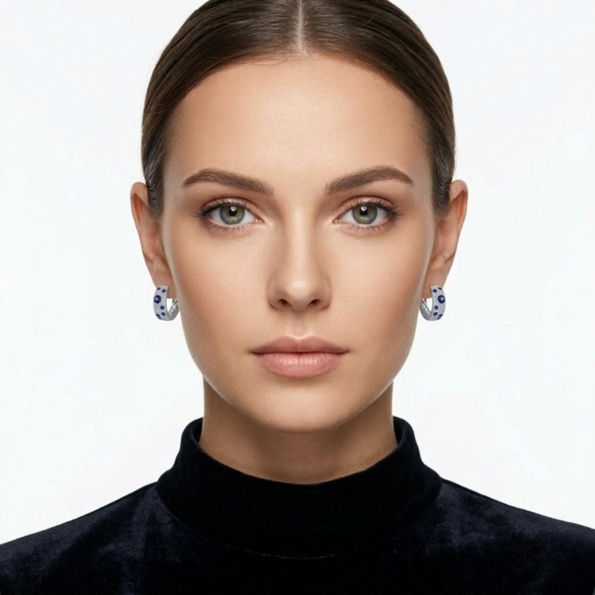 A close-up of a woman with her hair pulled back wearing the Kouvr Amaris sapphire and diamond hoop earrings, showcasing their scale and appearance when worn.
