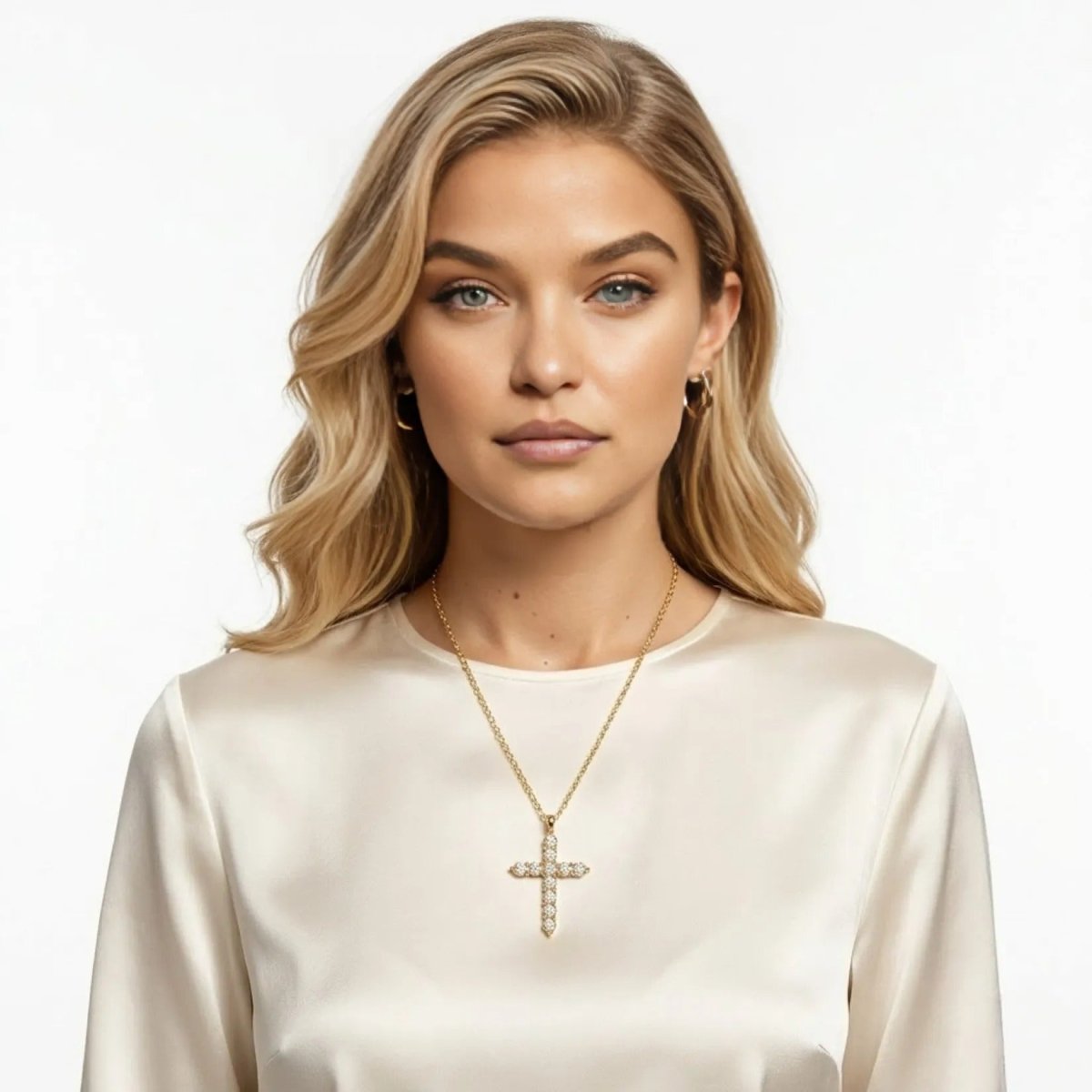 A woman with blonde hair wearing the Kouvr gold pave cross necklace with an elegant off-white silk blouse.
