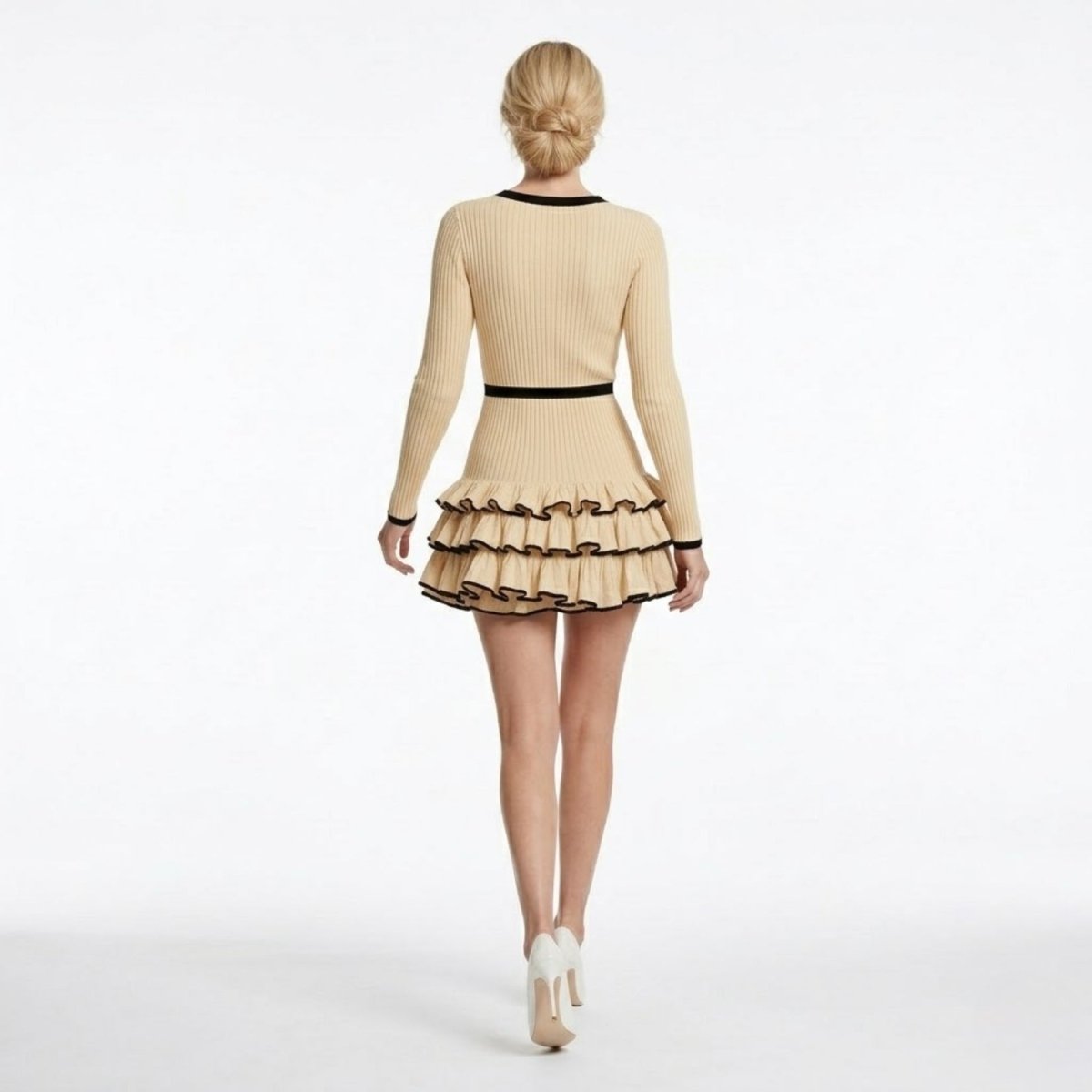 Back view of a beige long sleeve sweater dress featuring a cinched contrasting black waistband and voluminous tiered hem.
