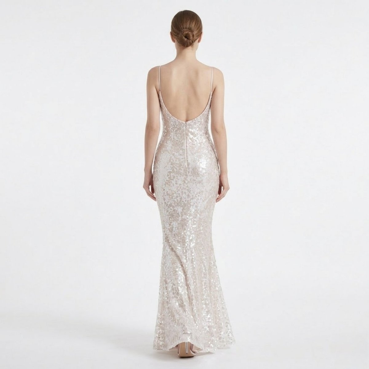 Back view of a female model wearing a backless white sequin formal dress, highlighting the deep V open back design and mermaid skirt flare.