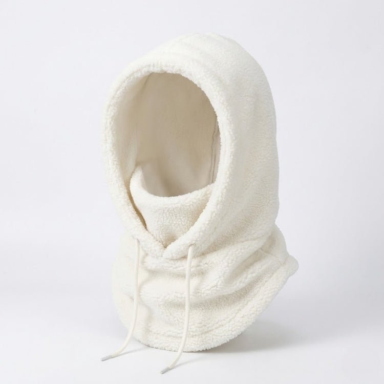 Model wearing a fitted white ski jumpsuit with fur trim and a matching white plush balaclava standing in a snowy mountain landscape.