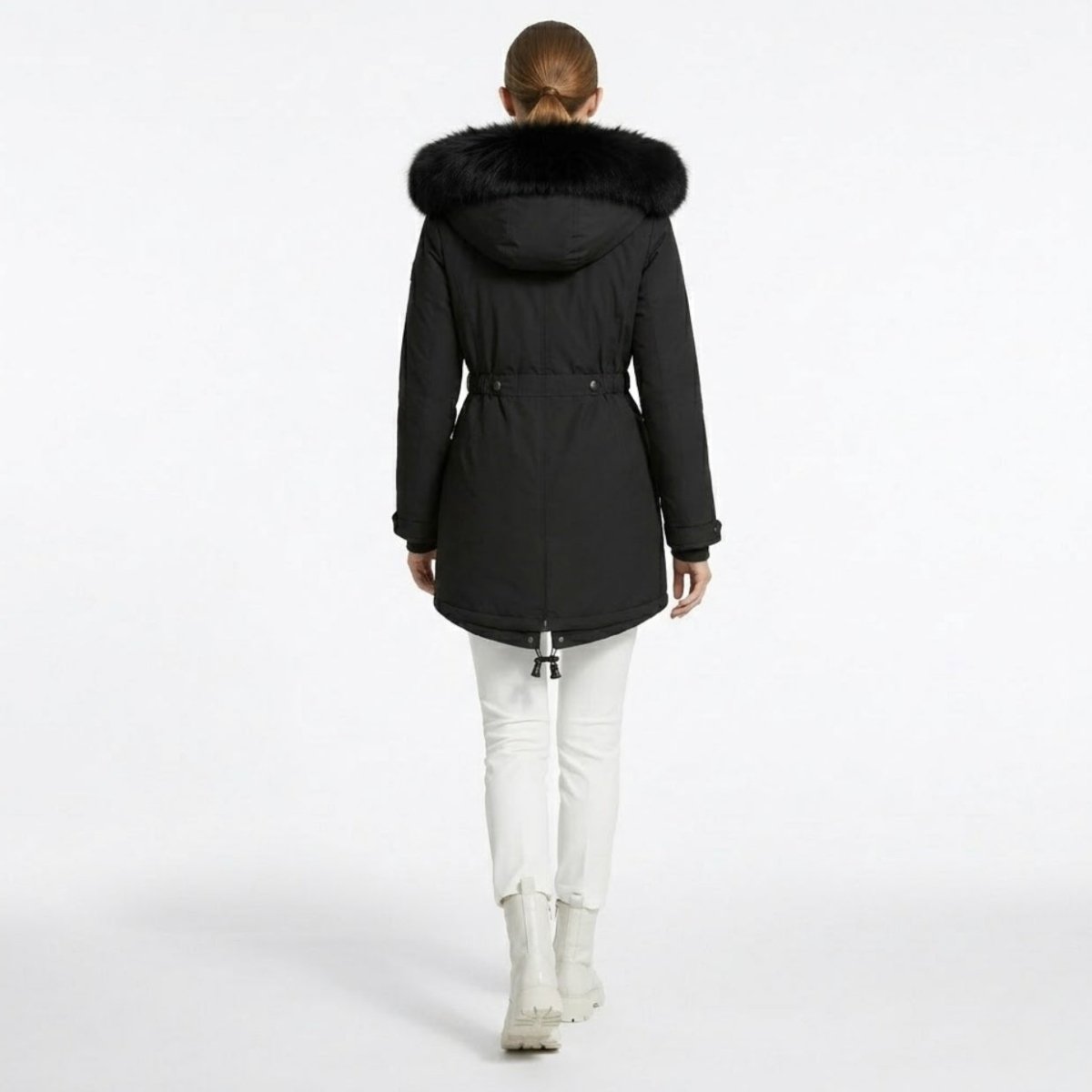 Back view of a woman wearing a black winter coat showing the cinched waist detail, large faux fur hood, and drop-tail hem.