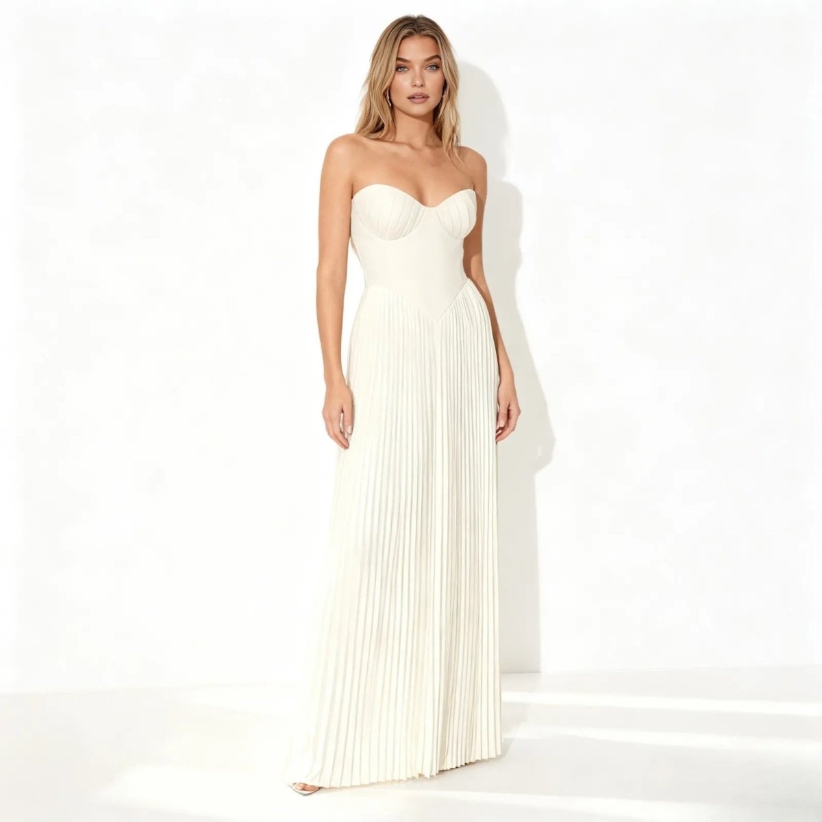 Woman wearing a strapless ivory kouvr pleated gown on a white background