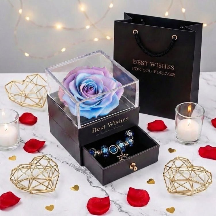A mystic blue and purple eternal rose displayed in a luxury black box with a silver charm bracelet, surrounded by rose petals.