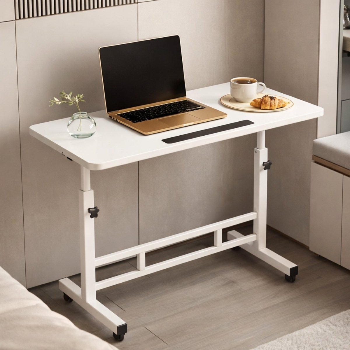 The Kouvr adjustable white C-table shown as a bedside desk with a laptop, coffee, and croissant, highlighting its use in a modern bedroom.