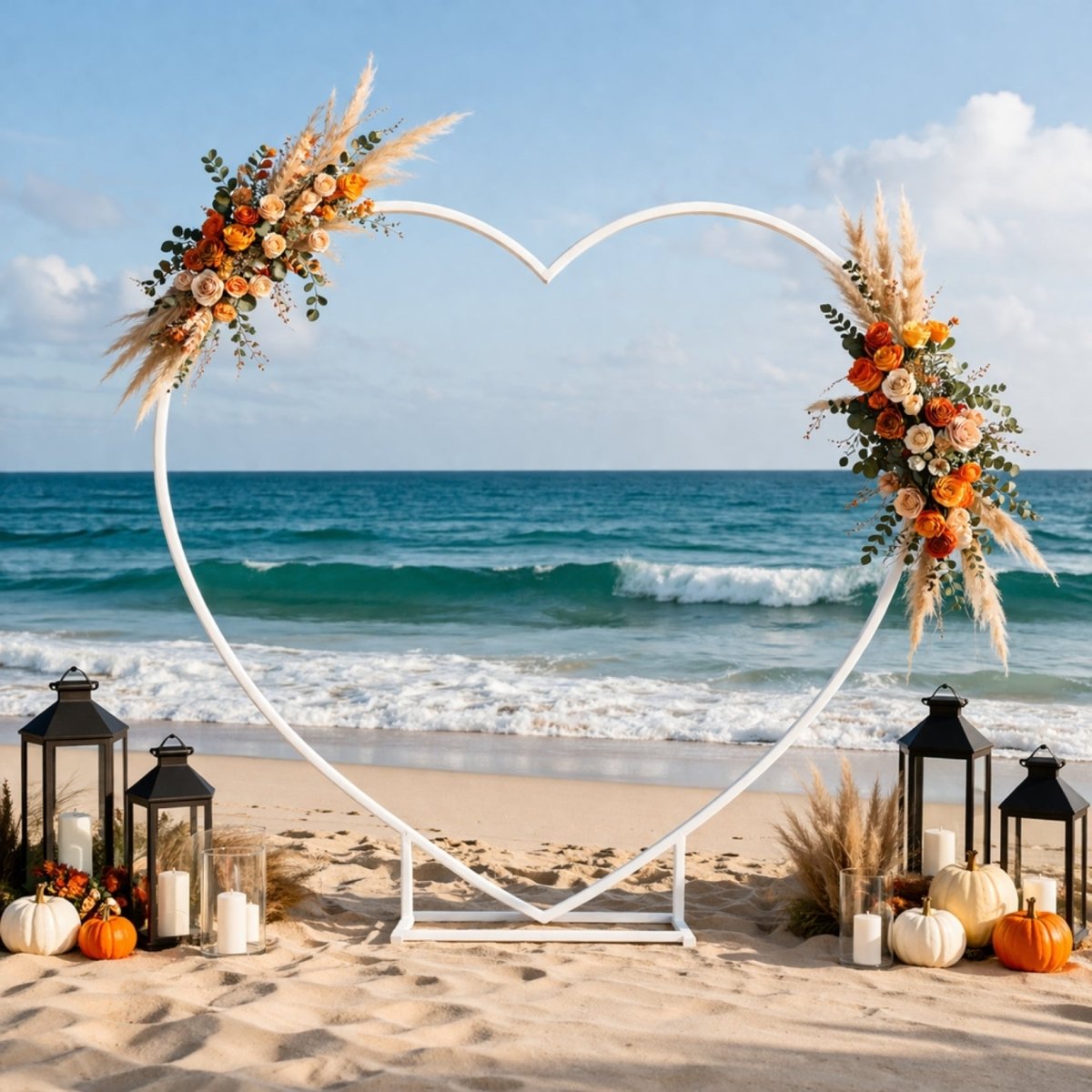 Fall themed beach event decor showcasing a white heart backdrop frame decorated with autumn florals, lanterns, and white pumpkins.
