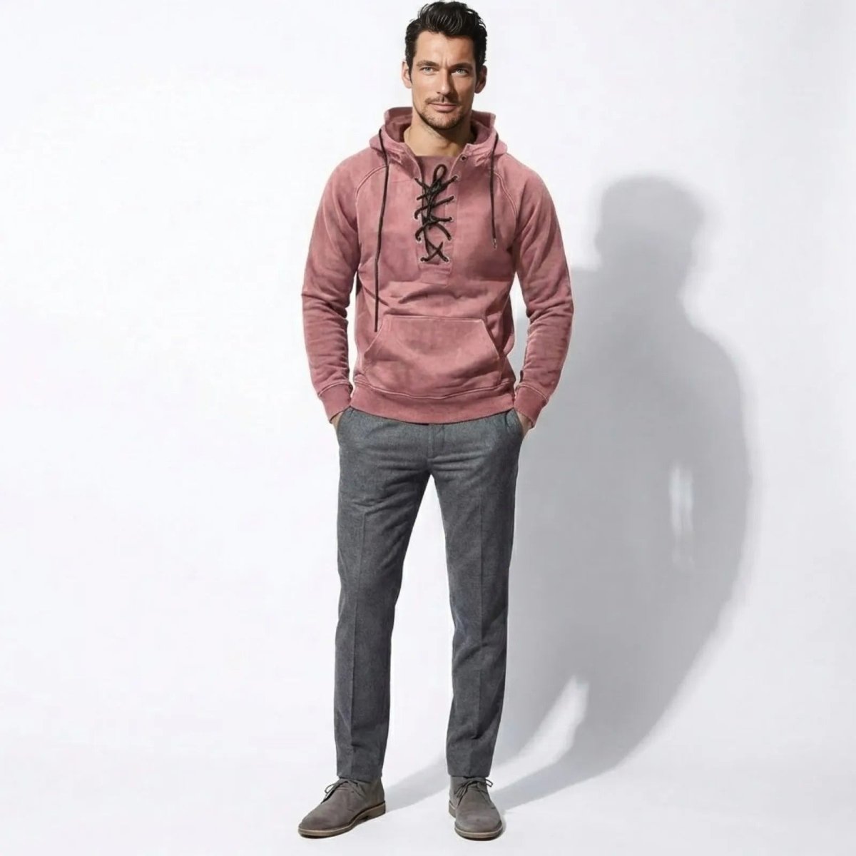 Man wearing the Kouvr Cannon Lace-Up Hoodie in pink, styled with grey trousers, shown from the front.