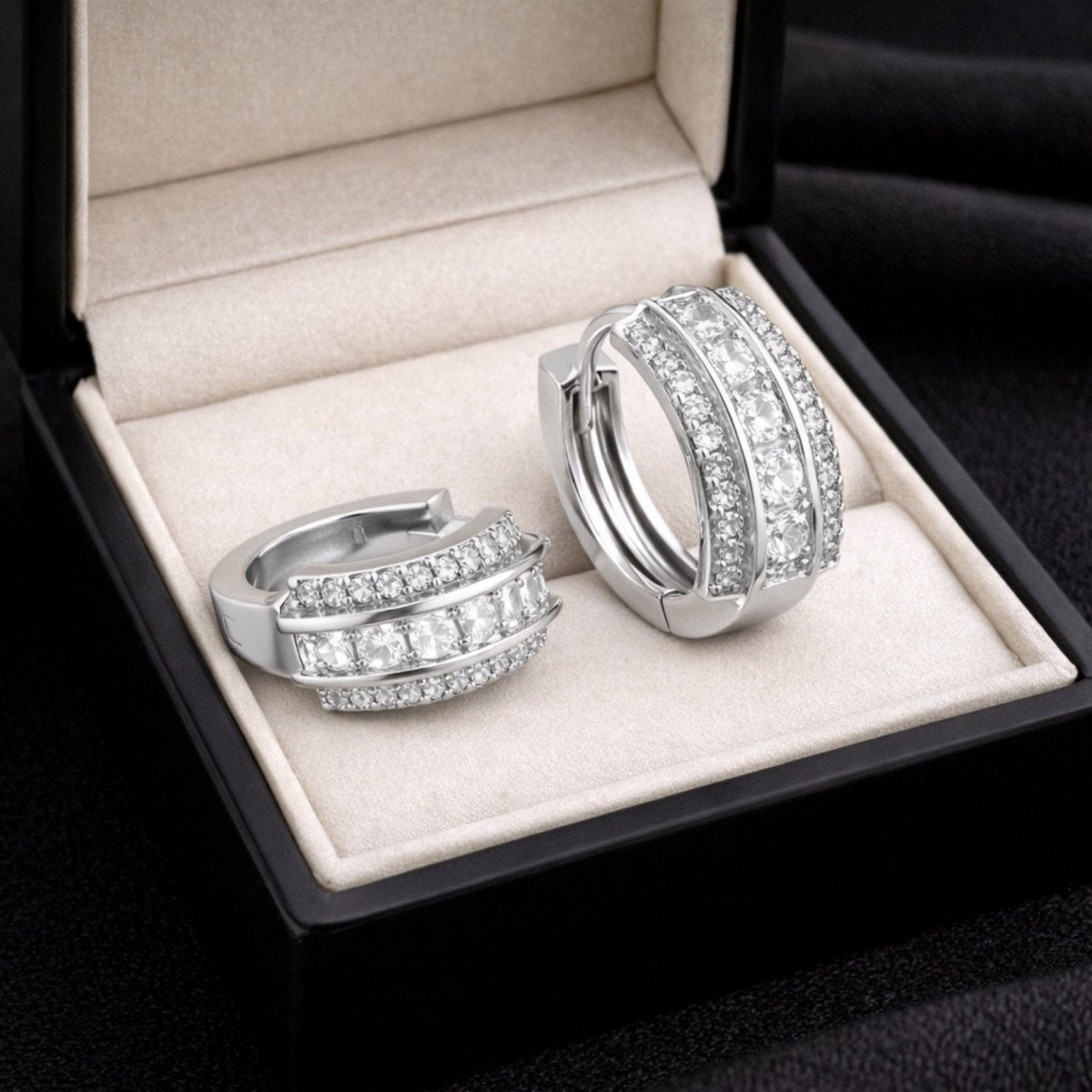 Close-up of one open and one closed princess cut diamond huggie hoop earring by Kouvr, resting inside a sophisticated black gift box.

