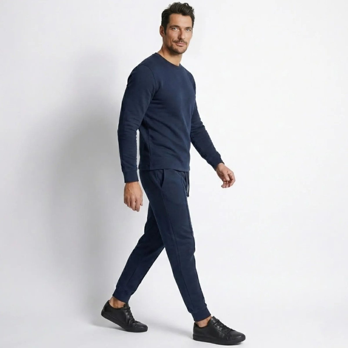 Side profile of a model walking in the Kouvr Crue  navy tracksuit, showcasing the garment's drape and slim silhouette.