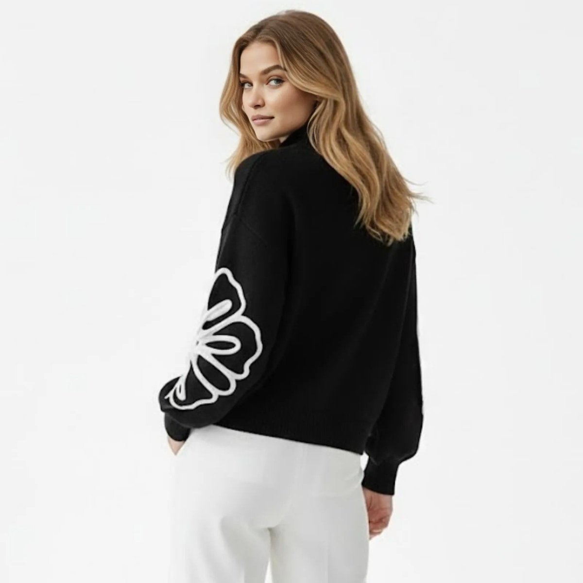 Back view of a model in the Kouvr Cynthia black mock neck sweater showing the elegant silhouette and floral detail on the left arm.