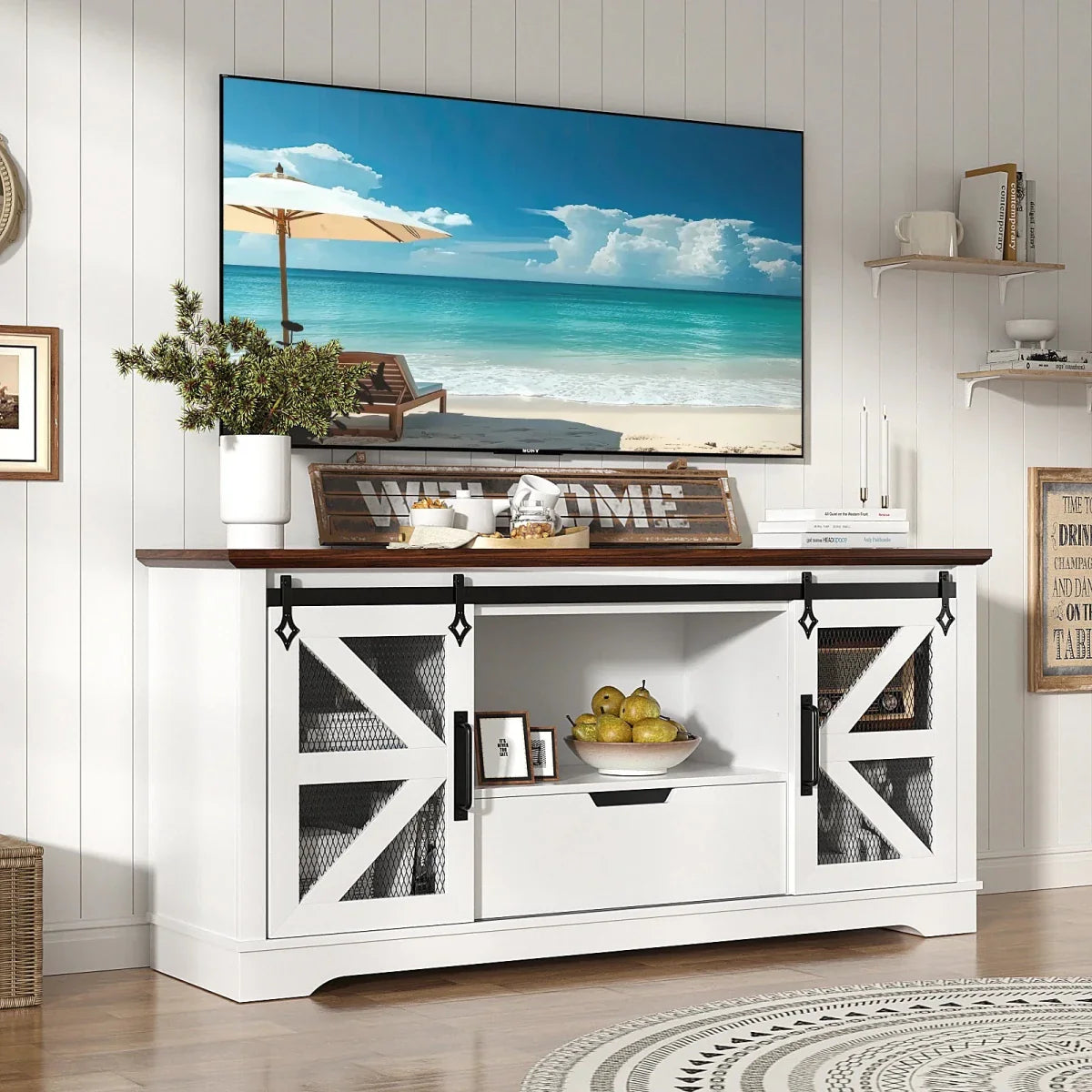 A 60-inch white and walnut farmhouse TV stand by Kouvr, featuring sliding barn doors with mesh, styled in a bright, modern living room with a large screen television.
 