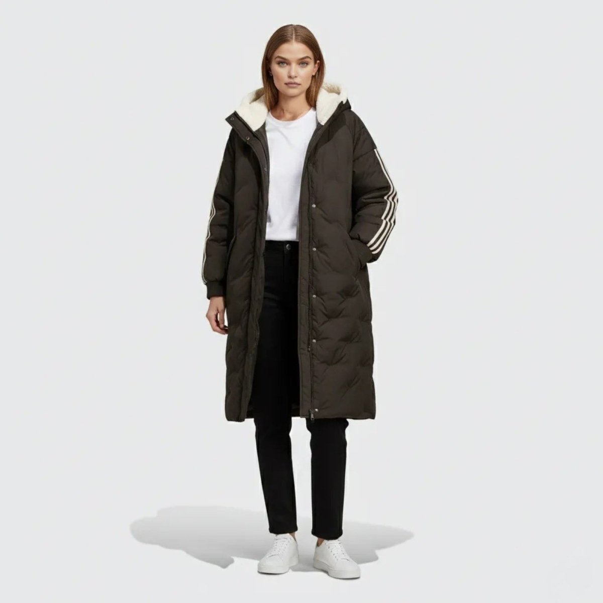 Model wearing the Kouvr Arianne long black puffer coat with a white sherpa-lined hood and three white stripes on the sleeve, shown from the front. 