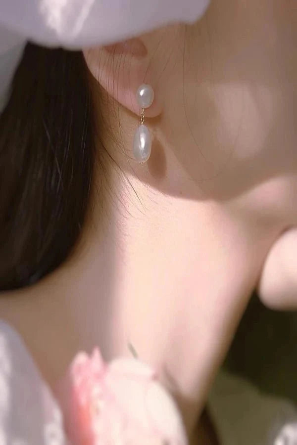 Close-up of a person wearing pearl Kouvr earrings with a soft focus background