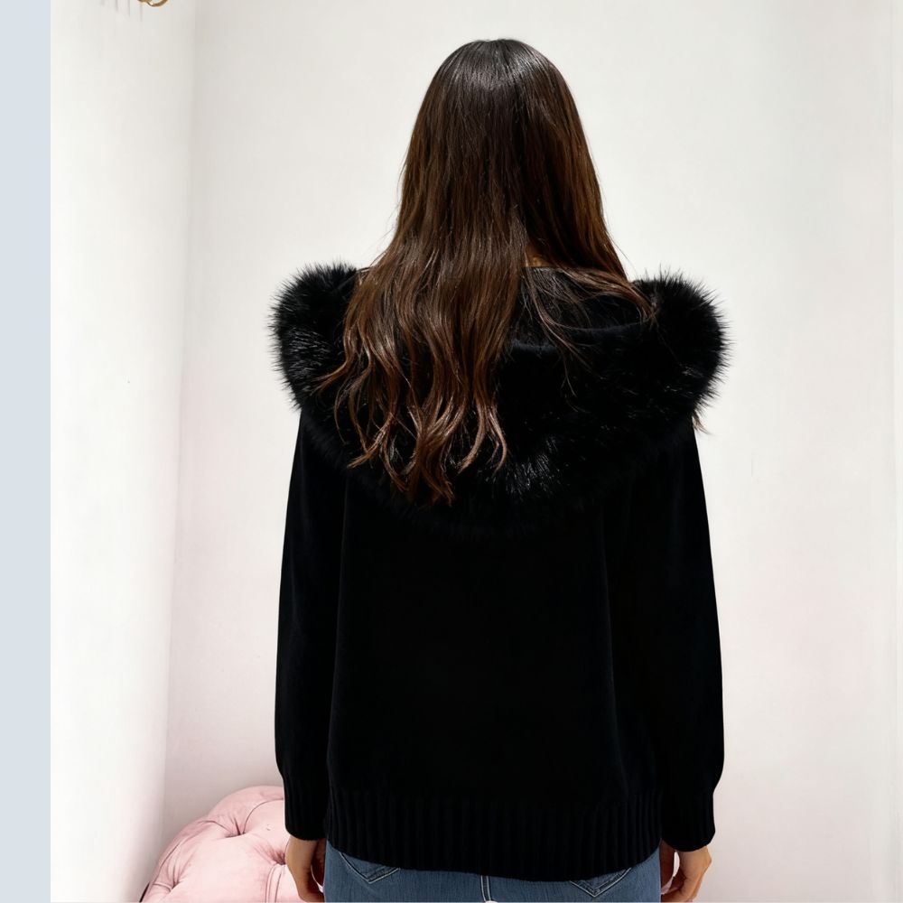 Person wearing a black kouvr  coat with fur trim, standing against a plain background