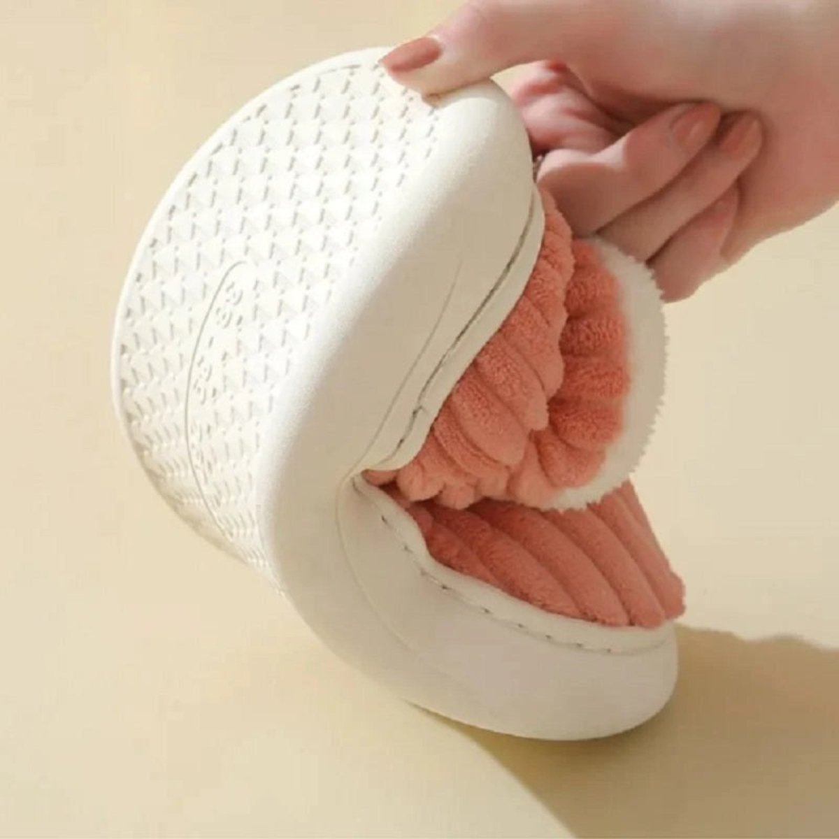A hand bending the flexible, durable white EVA sole of the pink Jasmine corduroy slipper to demonstrate its quality and comfort. 
