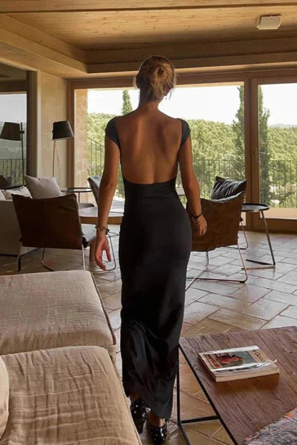 Model wearing the Kouvr Grace black boat neck maxi dress with a full view of the open back