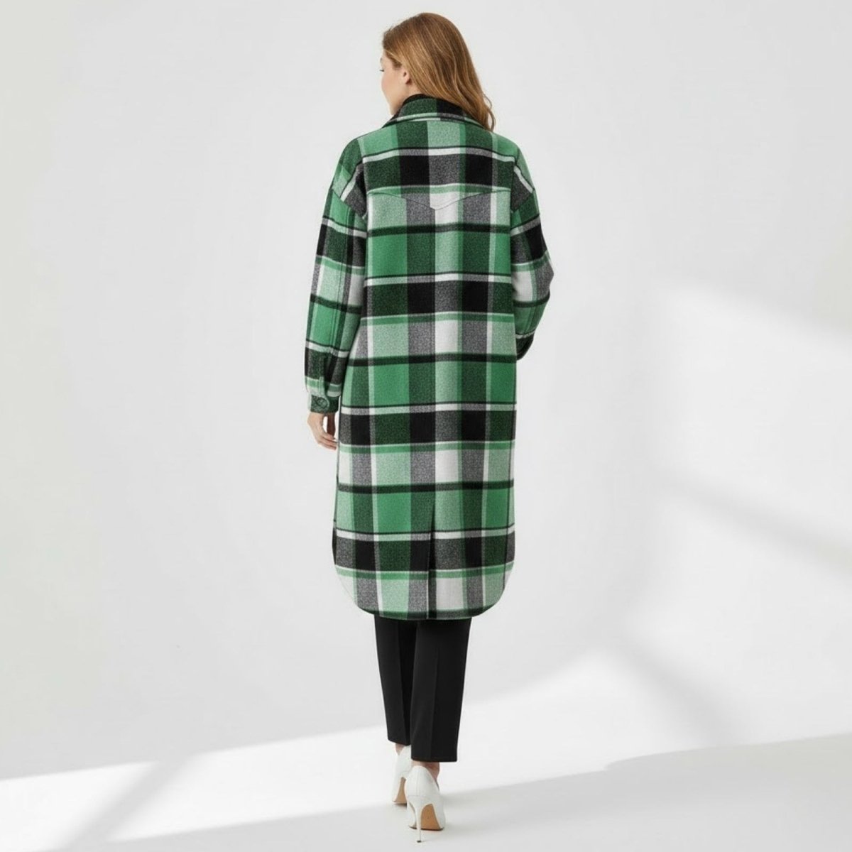 Back view of a model in the Kouvr green check overcoat, showing the shoulder yoke and full length of the plaid pattern.