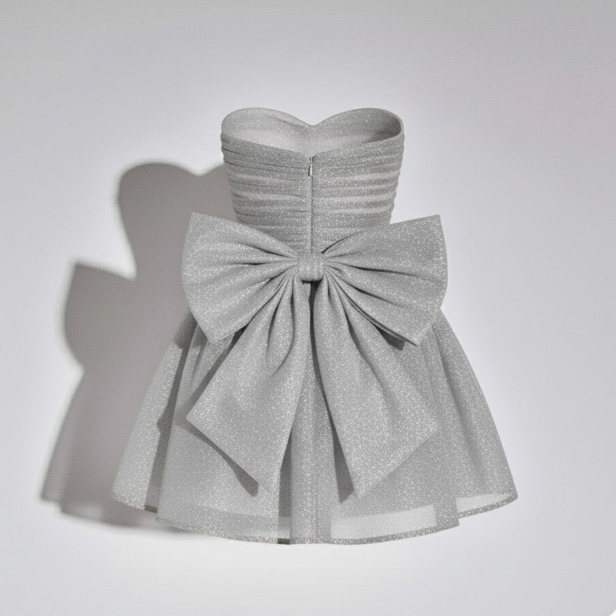 Back product shot of the Kouvr Harmoni silver mini dress showing the oversized glitter bow on a ghost mannequin.