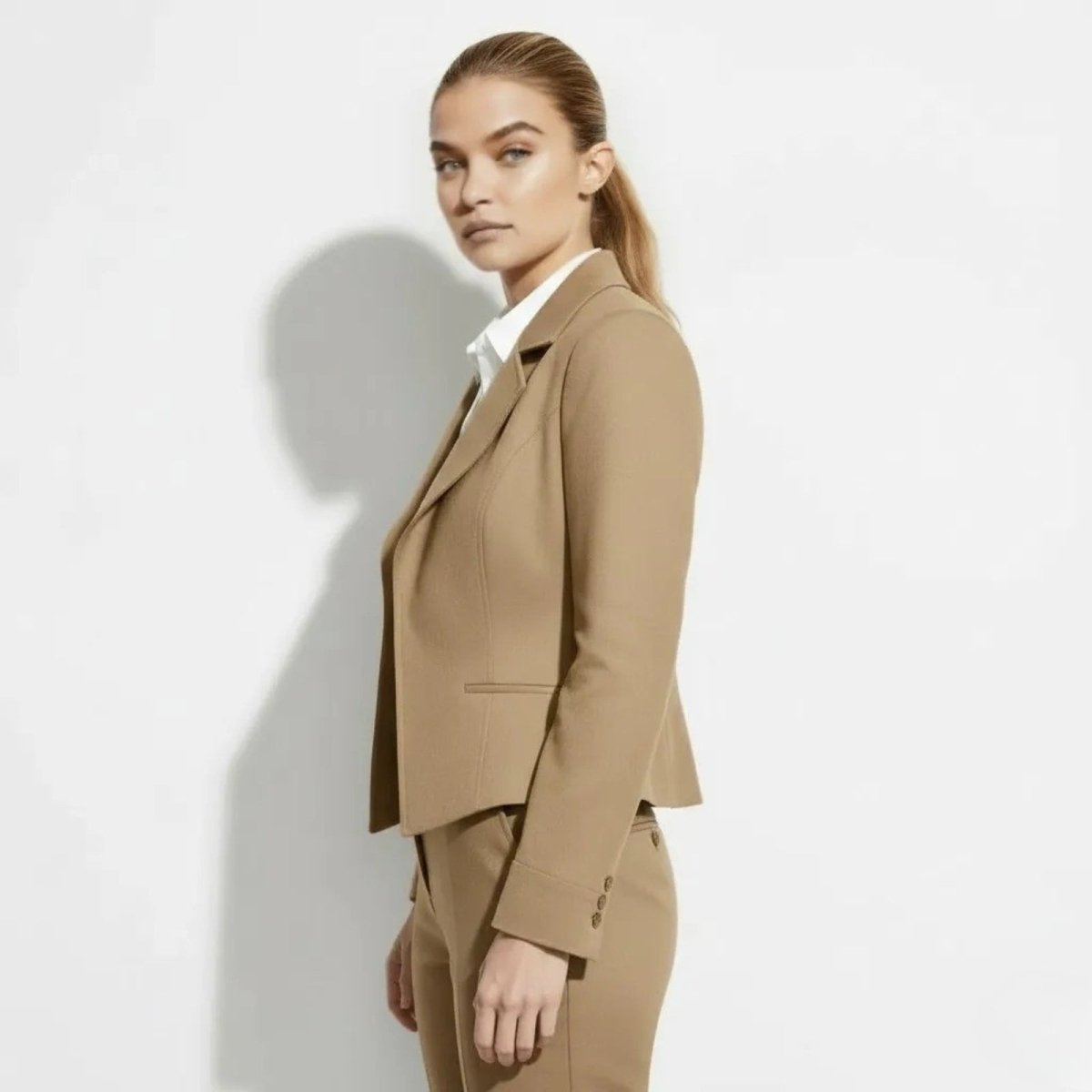 Side view of a woman in a fitted tan structured blazer from Kouvr, highlighting the cropped length and three-button cuff detail.