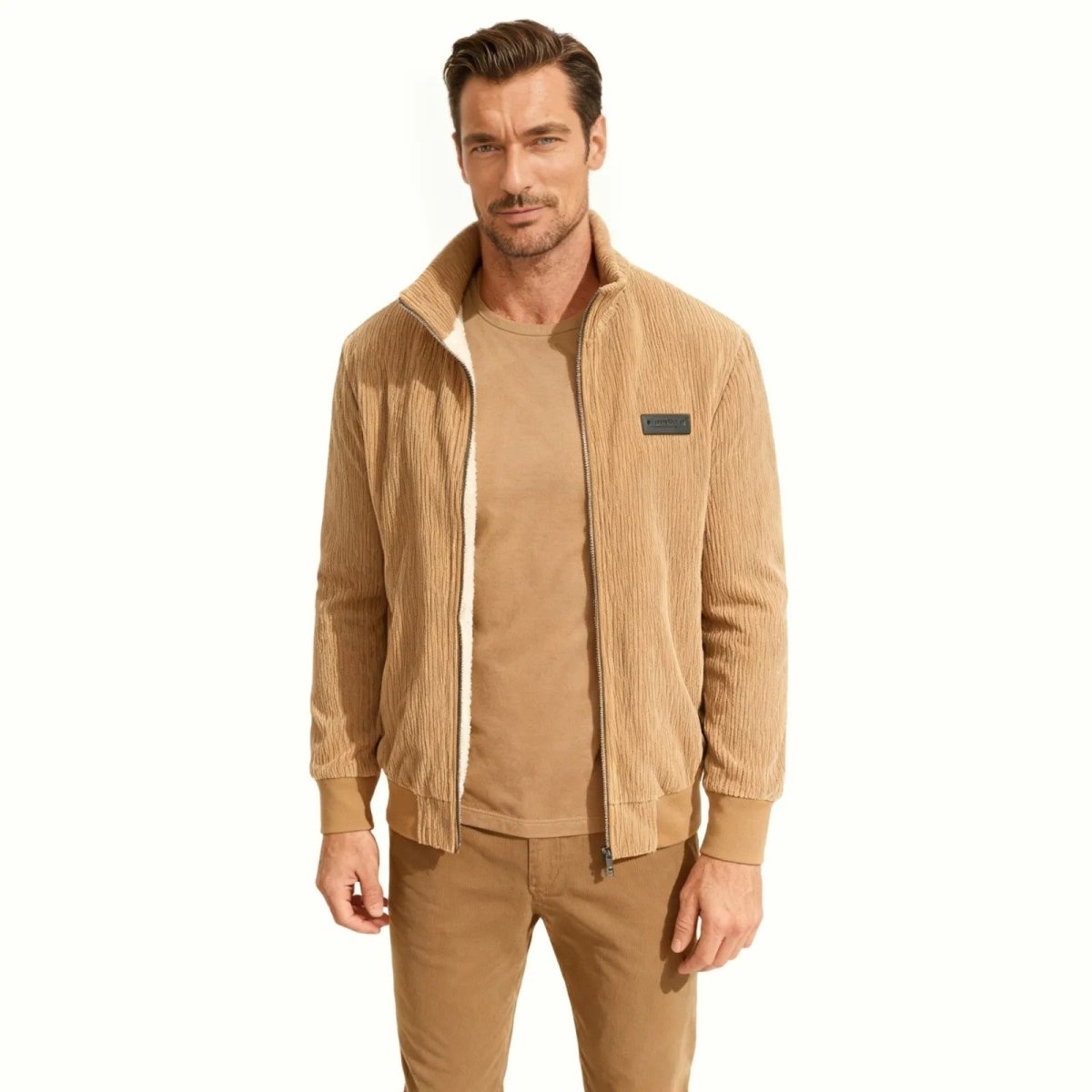 A male model wearing the Kouvr beige corduroy sherpa-lined bomber jacket, viewed from the front, styled with a matching t-shirt and trousers.