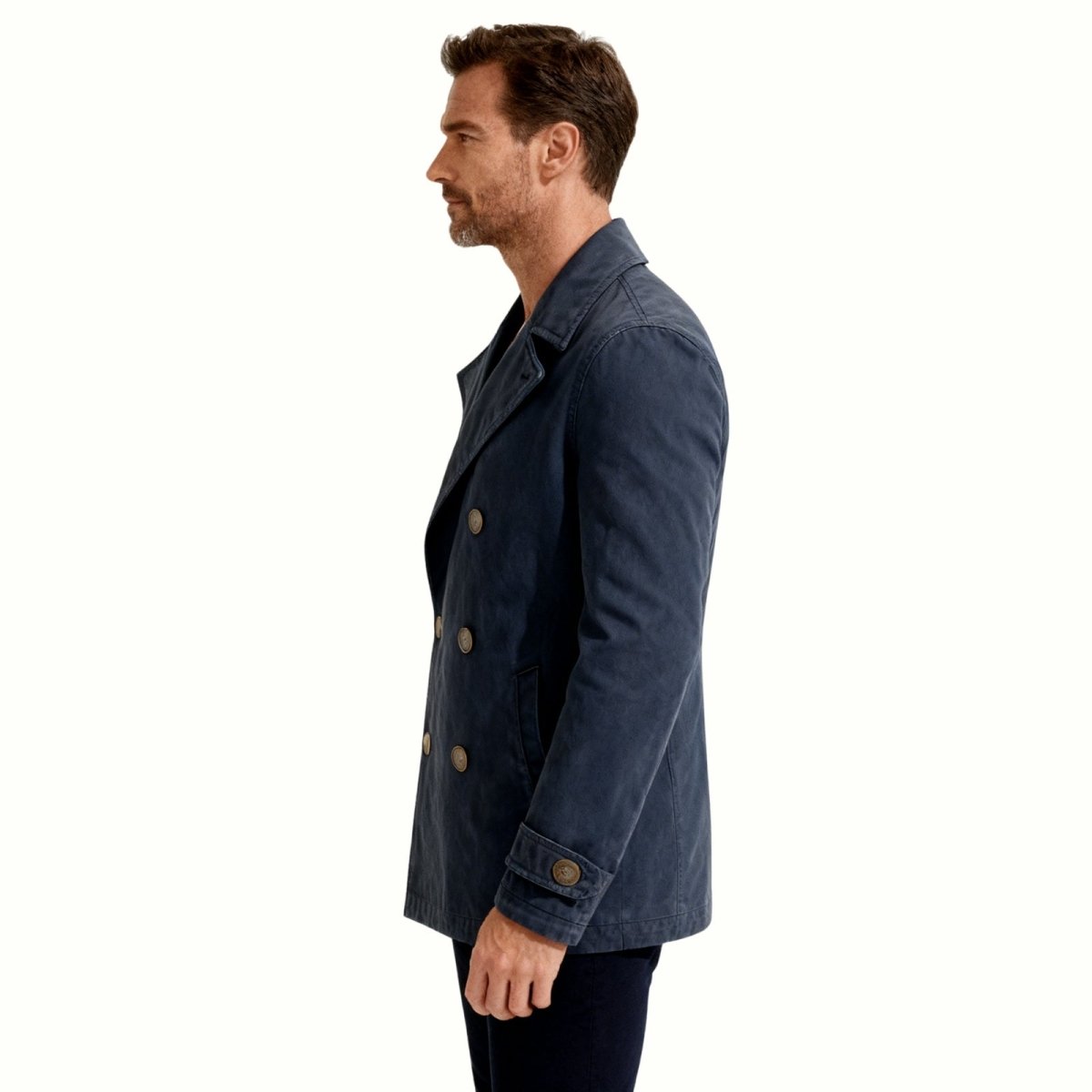 Side profile view of a man wearing the Kouvr navy blue double-breasted cotton peacoat to show its length and silhouette.