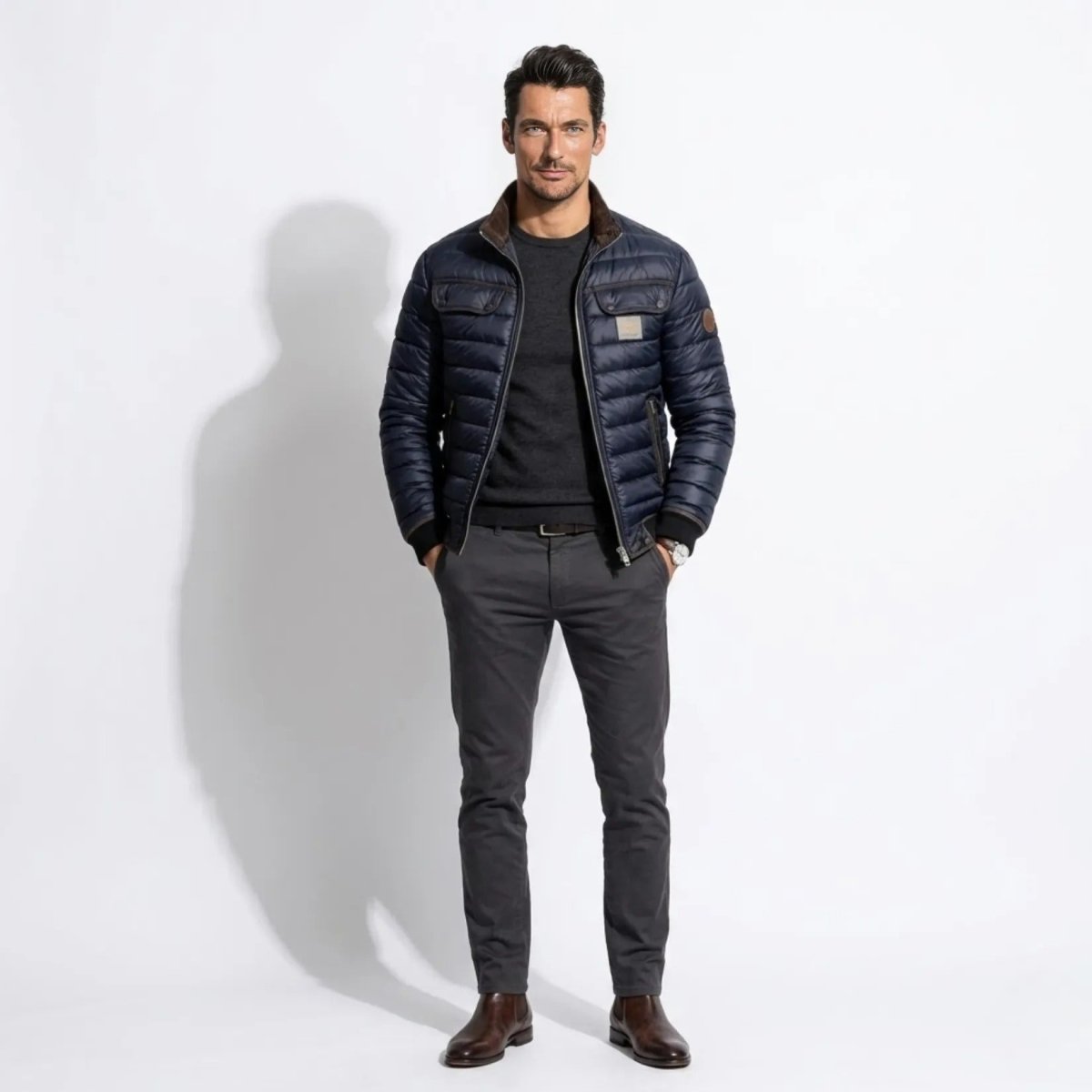 Front view of male model wearing the Kouvr navy blue quilted bomber jacket with smart casual grey trousers.