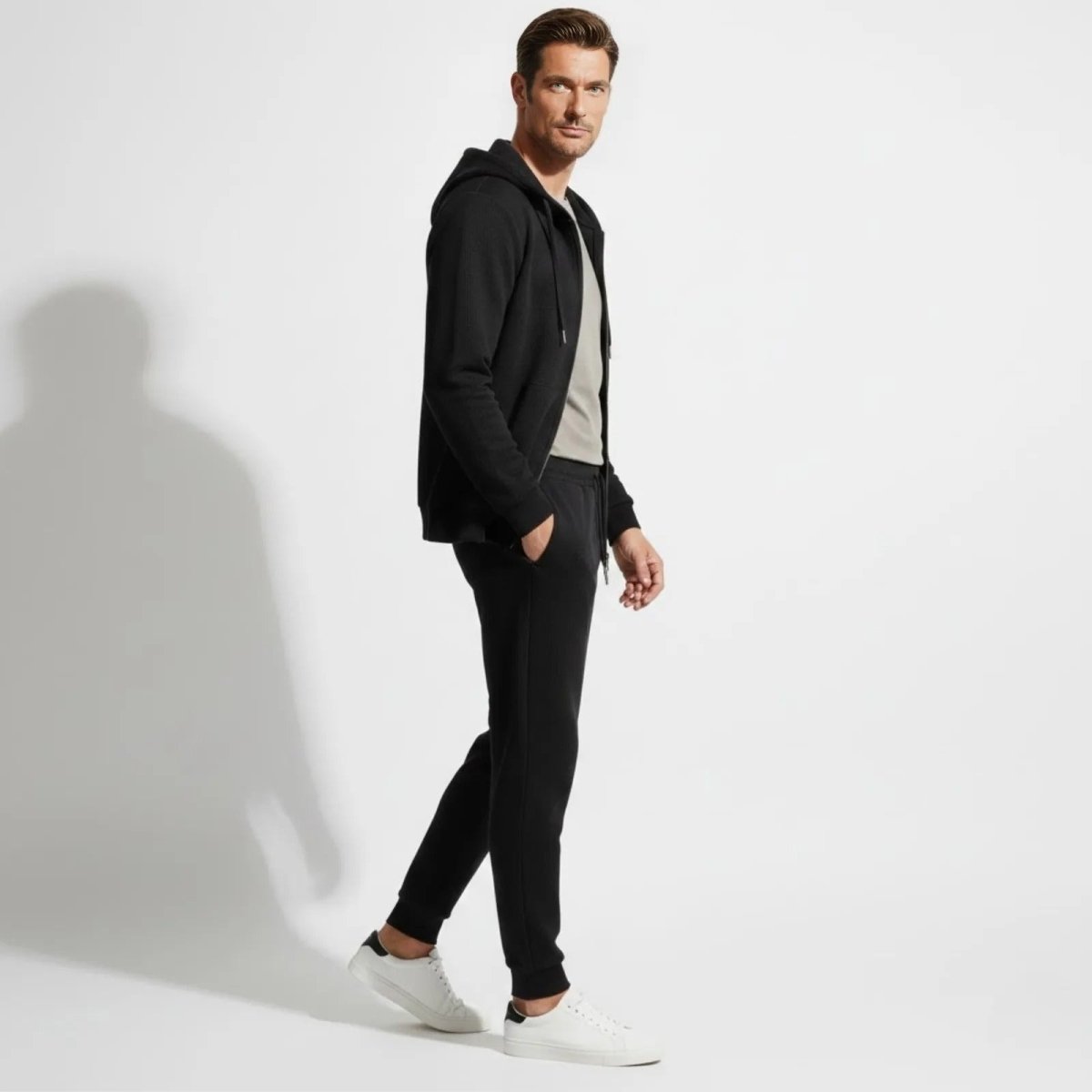 Side profile of a male model walking in the Kouvr black waffle-knit zip hoodie and jogger pants, showcasing the slim fit.