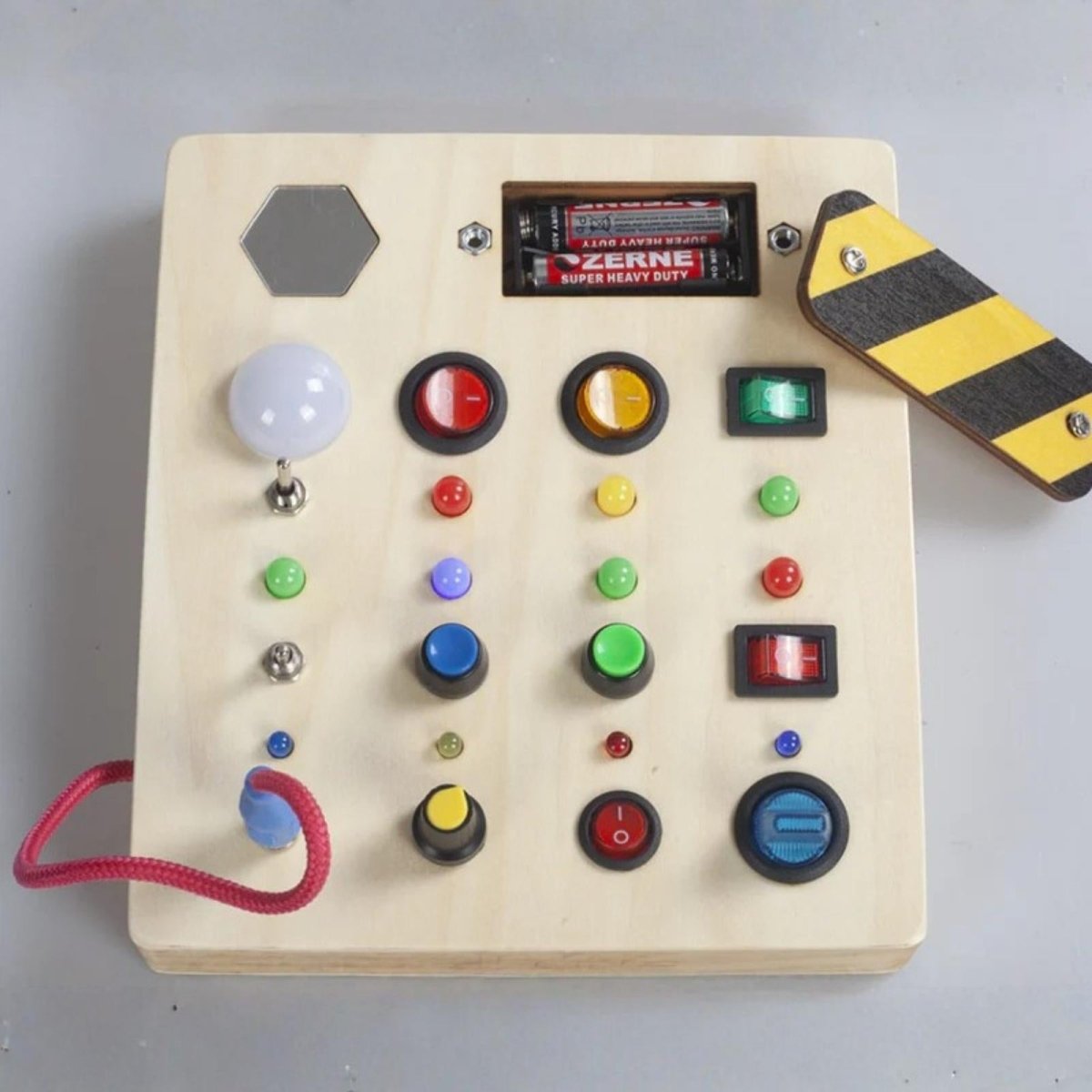 Top-down view of the Kouvr wooden busy board for toddlers, showing all features including the secure battery compartment with two AAA batteries.