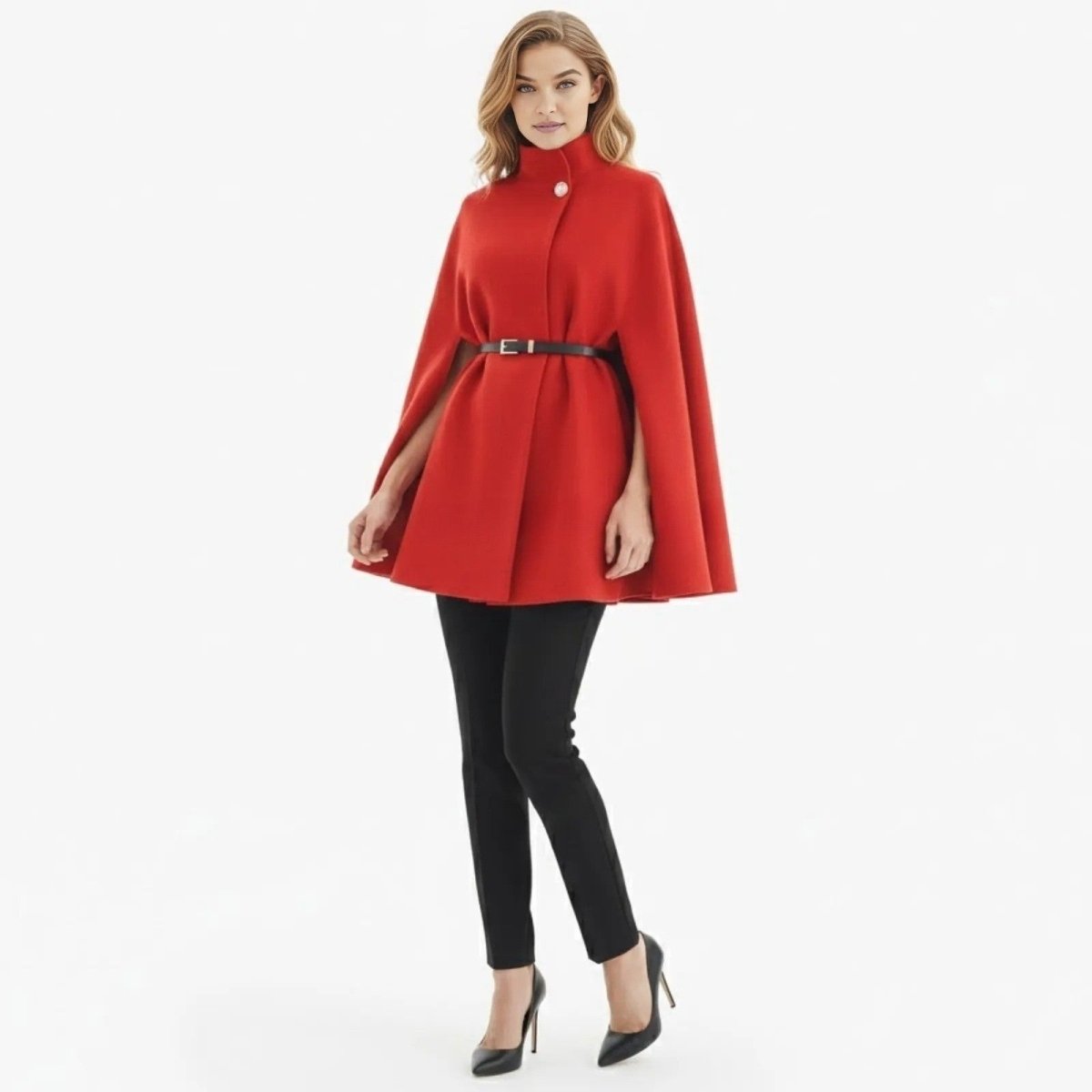 Female model facing forward wearing the Kouvr red high-neck cape coat, cinched with a black belt, paired with black trousers and heels against a white background.