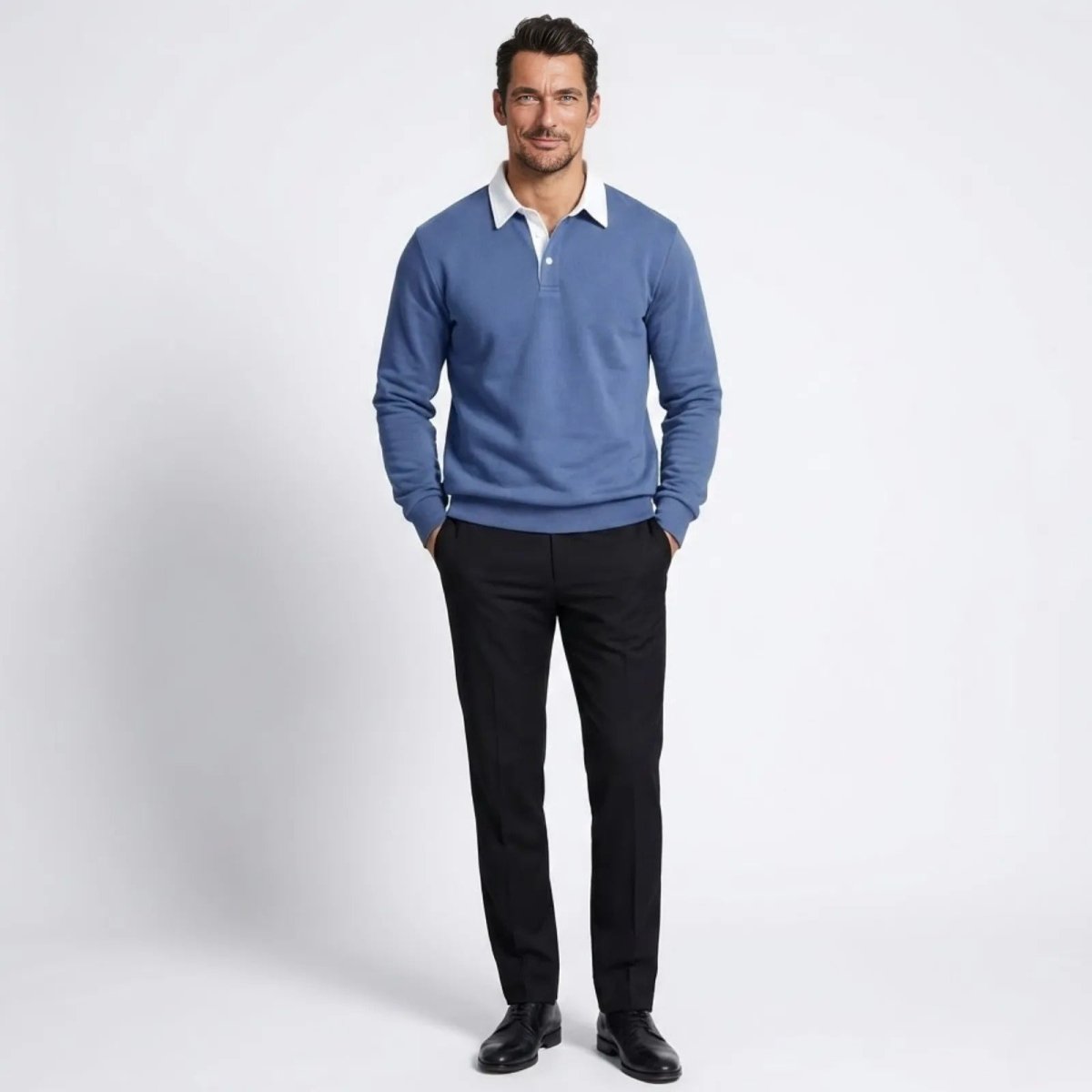 Man wearing the Kouvr Rhodes long sleeve polo sweater in steel blue, styled with black dress pants and black shoes, standing against a white background.