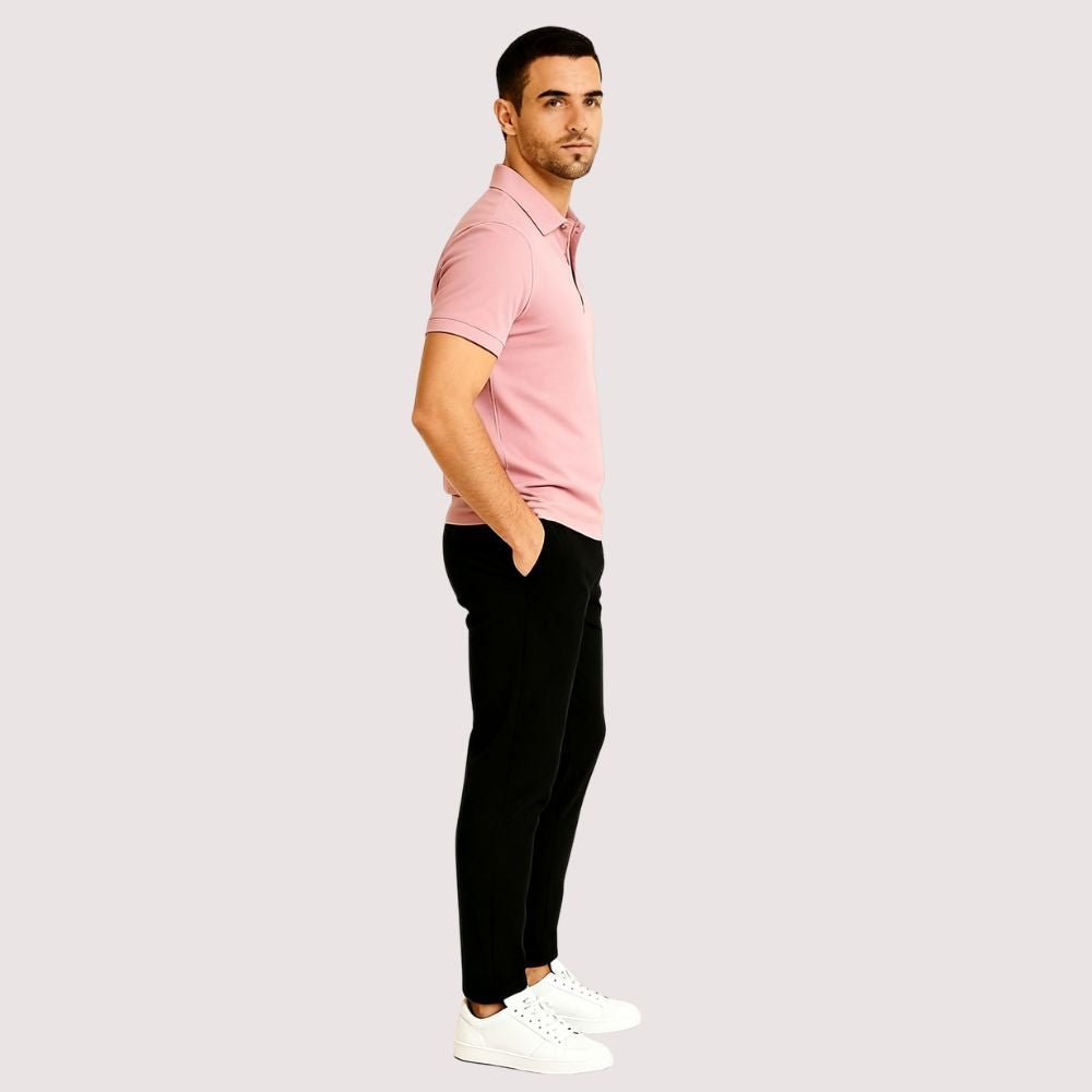 Man wearing a pink kouvr polo shirt and black pants on a light gray background