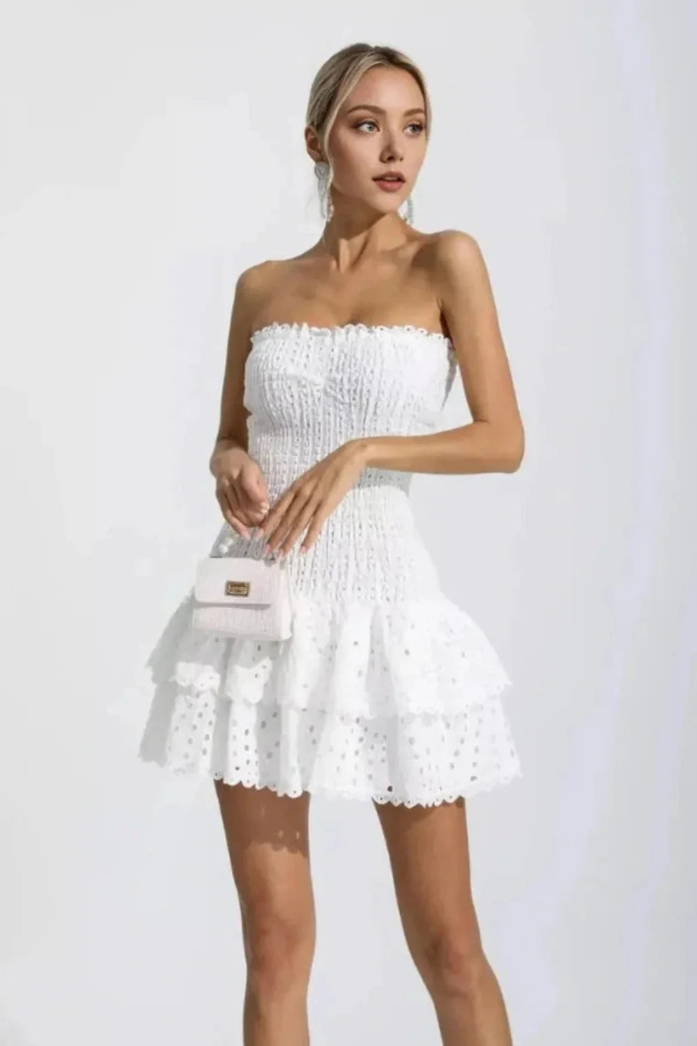 Model wearing the Kouvr Starla white strapless smocked mini dress with a tiered broderie anglaise ruffle skirt