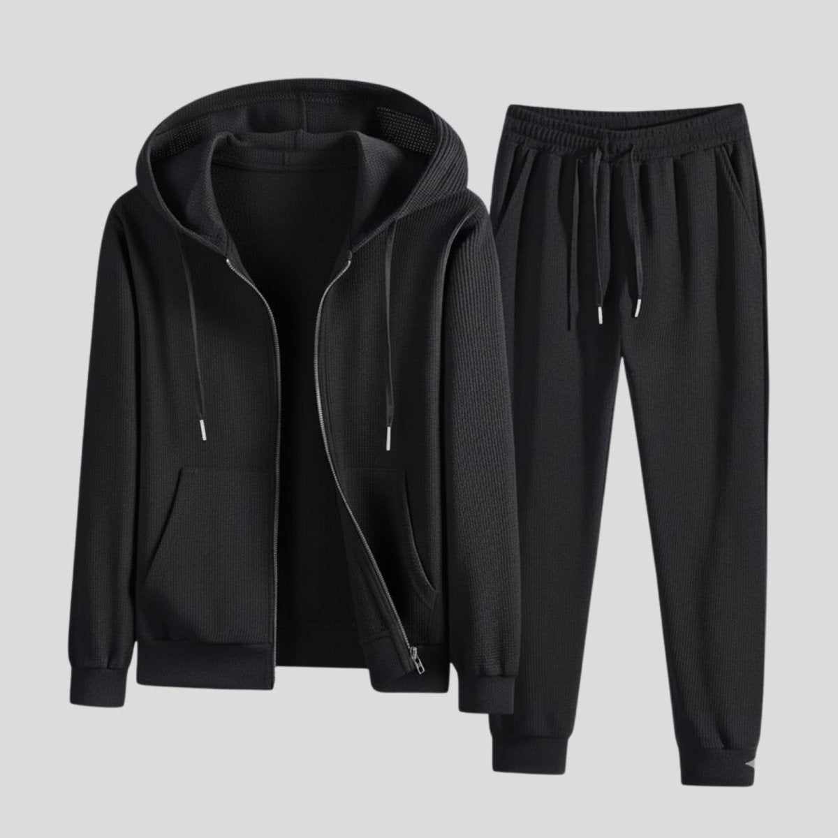 Flat lay of the Kouvr men's waffle-knit tracksuit in black, with the zip hoodie open to show the interior and the joggers placed neatly beside it.