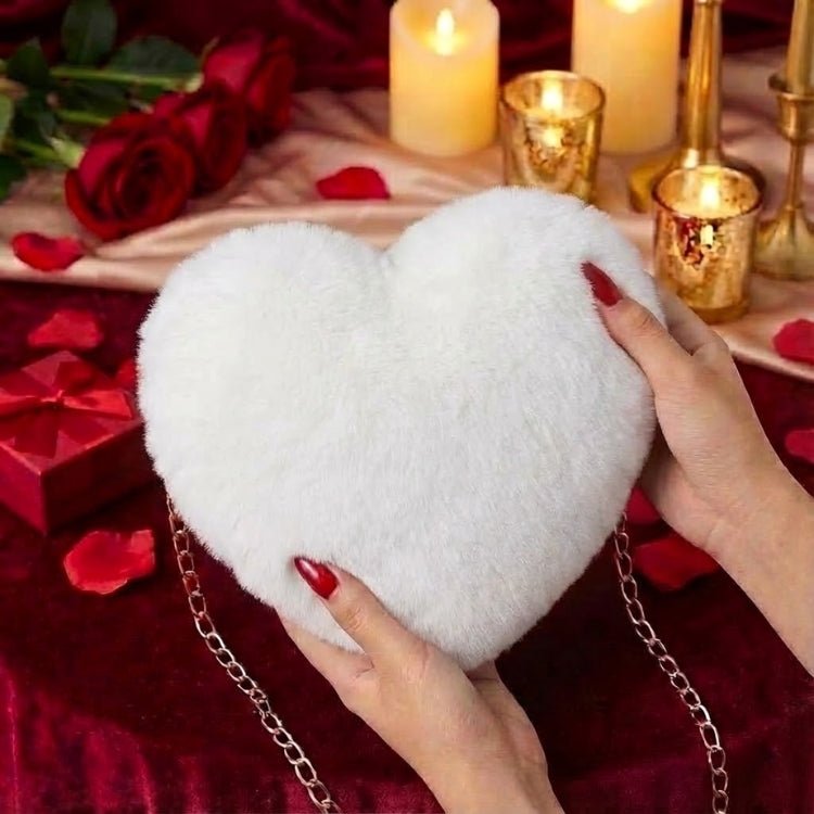 Hands with red nails holding the Kouvr white faux fur heart-shaped clutch against a romantic red velvet background with candles