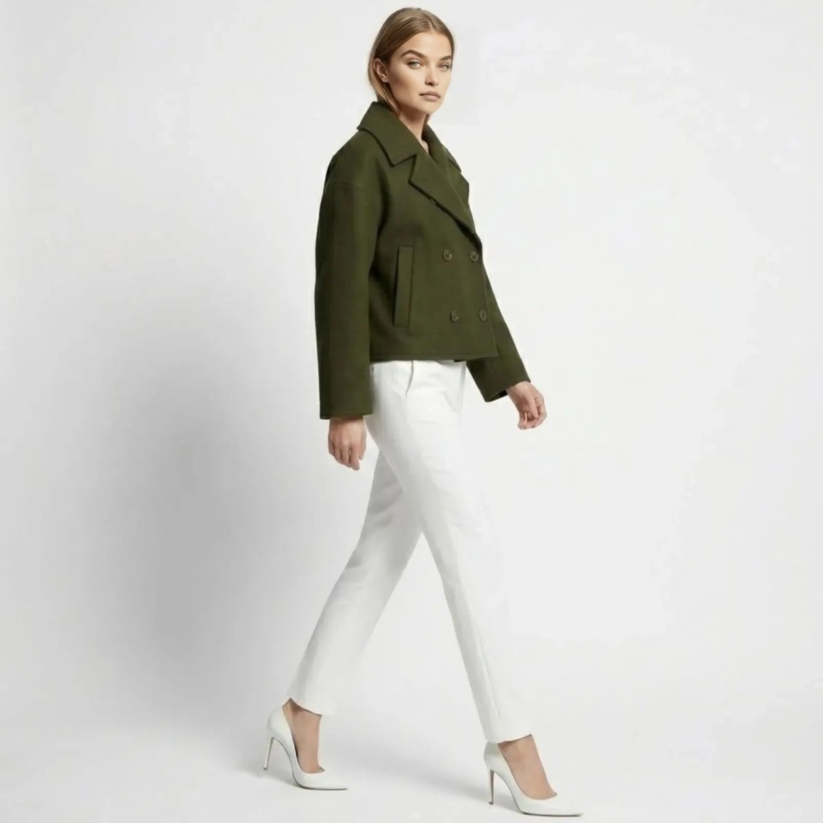 Side profile of a model walking in the Kouvr dark green cropped peacoat, showing its boxy silhouette and sleeve length.
