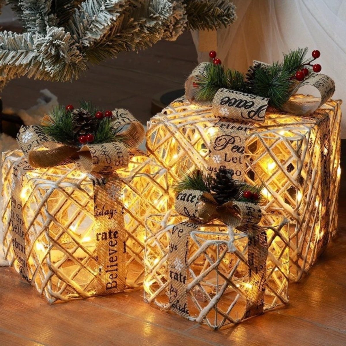 A close-up of three rustic woven lighted Christmas gift boxes wrapped in burlap ribbons with the words Peace and Believe, placed on a wood floor.