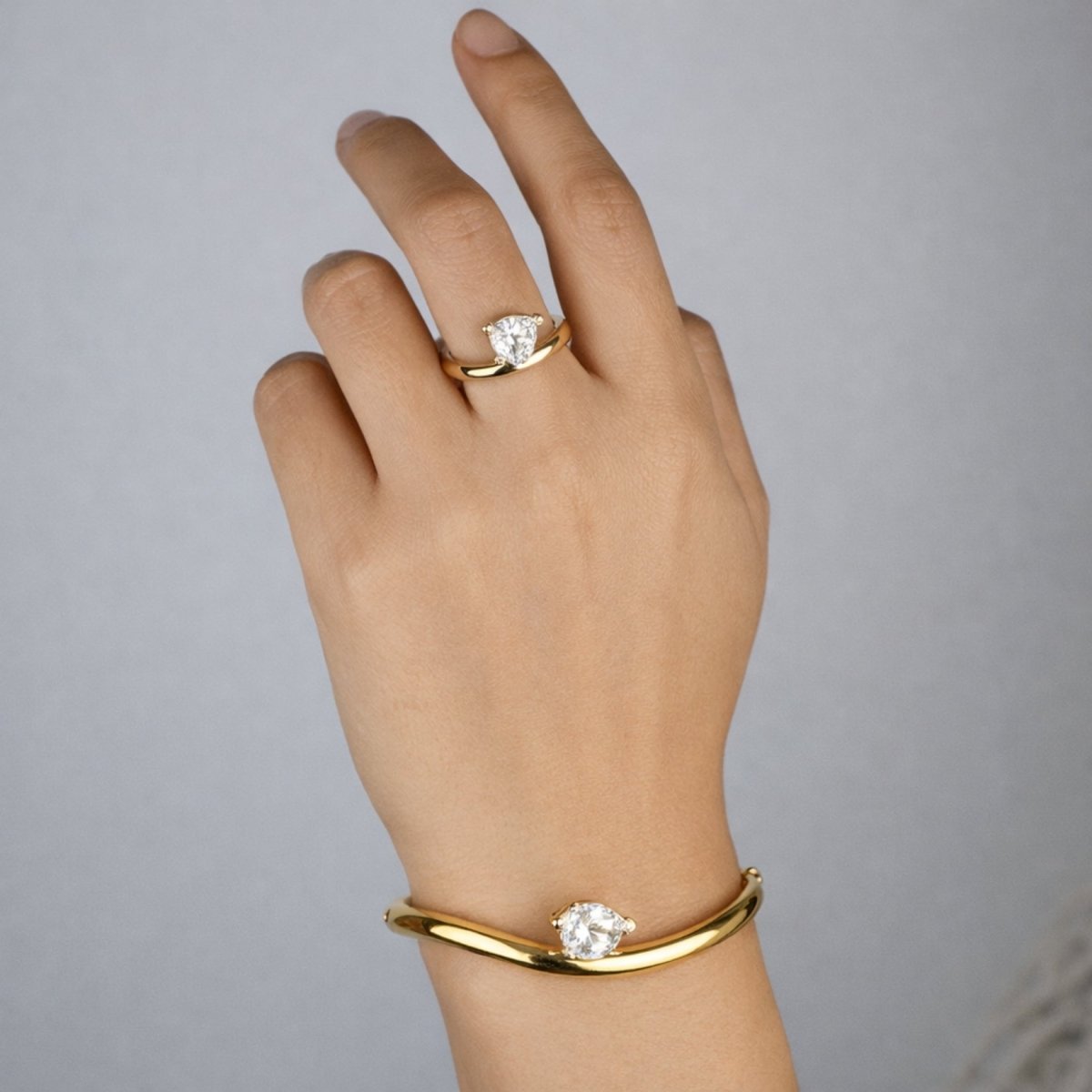 A model's arm raised, showcasing the Kouvr Yelena gold wave bangle and matching pear-cut solitaire ring. 