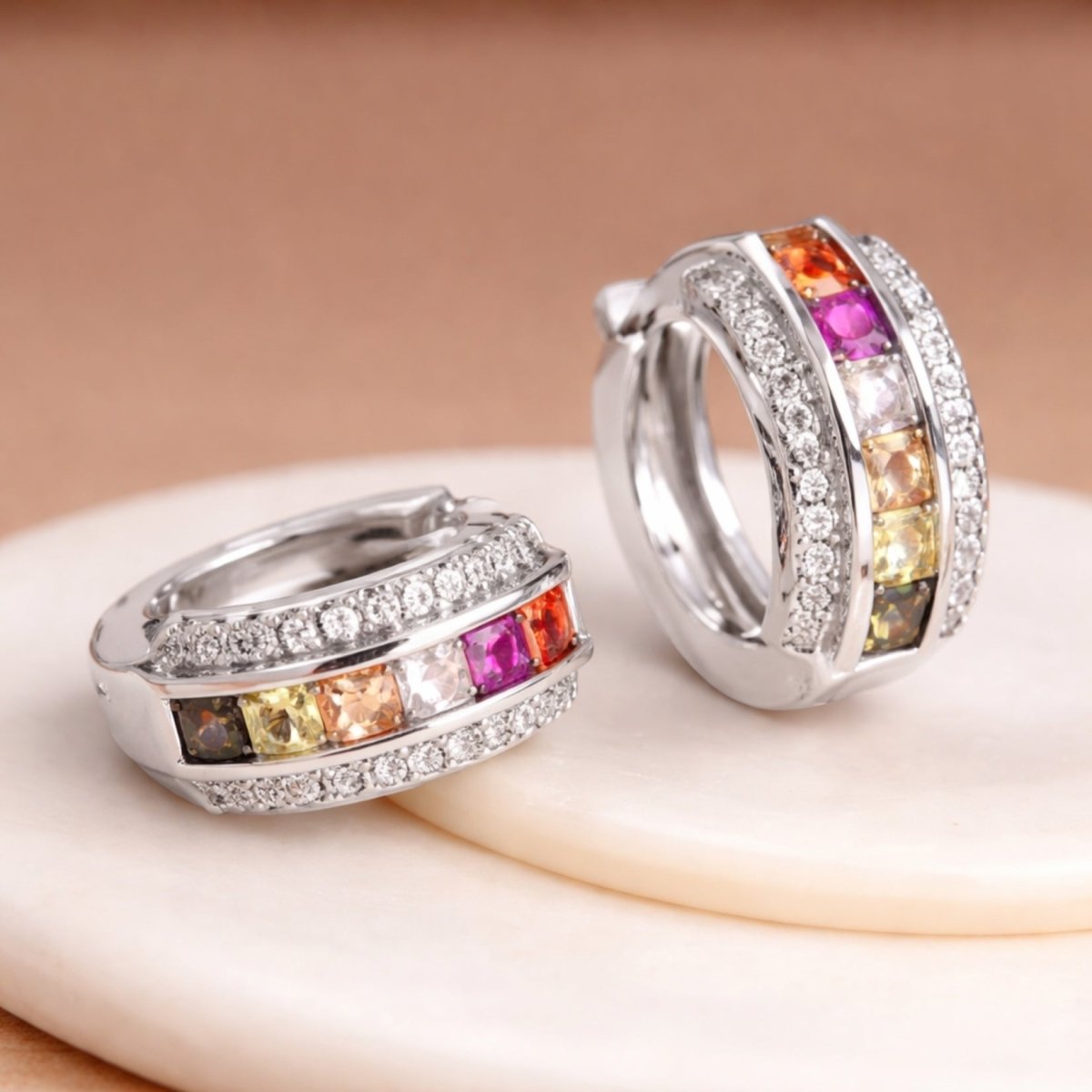 An angled view of the Kouvr Zinia  rainbow sapphire earrings on a white marble surface, showcasing the craftsmanship and diamond pavé details.