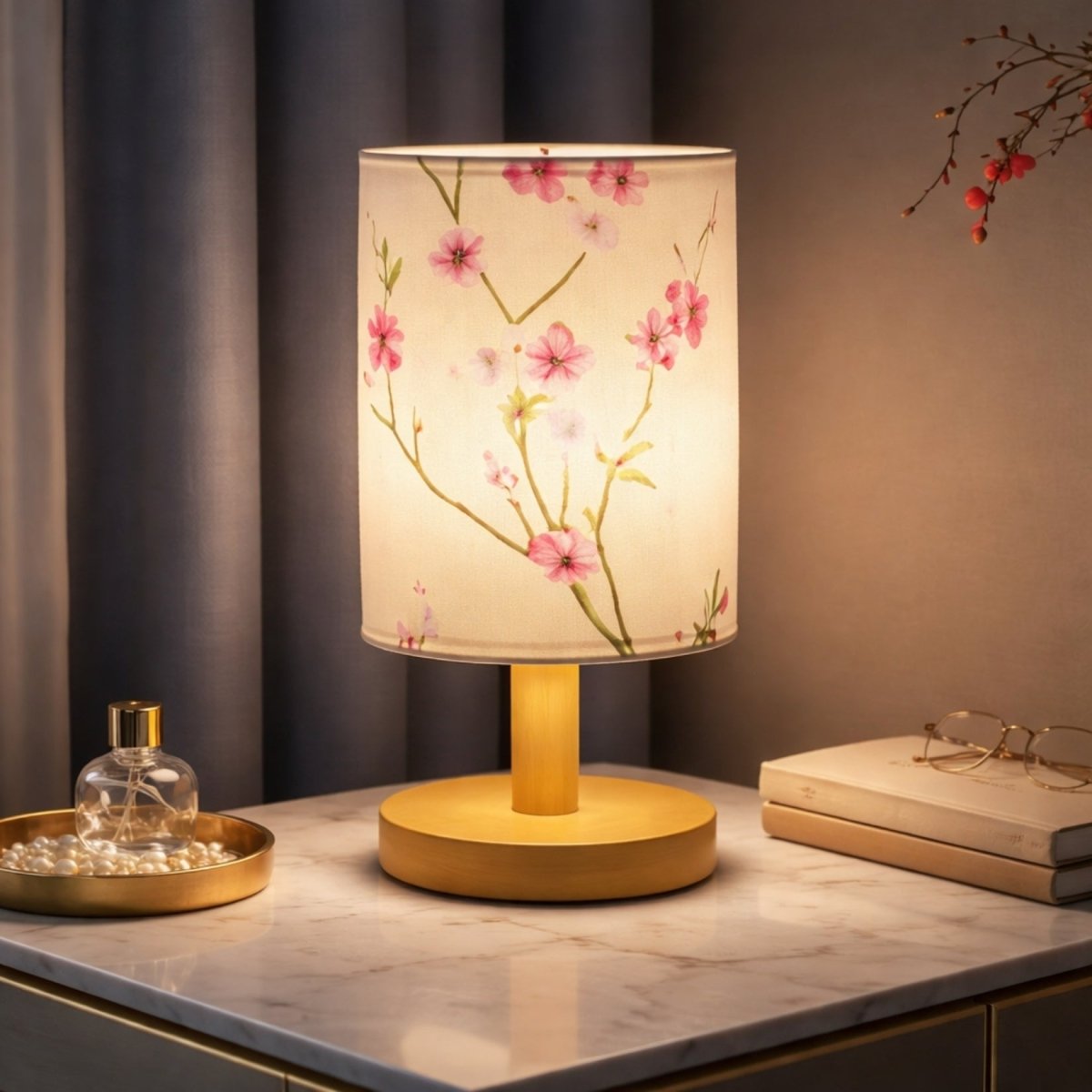 Kouvr dimmable wood table lamp with delicate pink cherry blossom design, creating warm ambient lighting on a luxury marble bedside nightstand.

