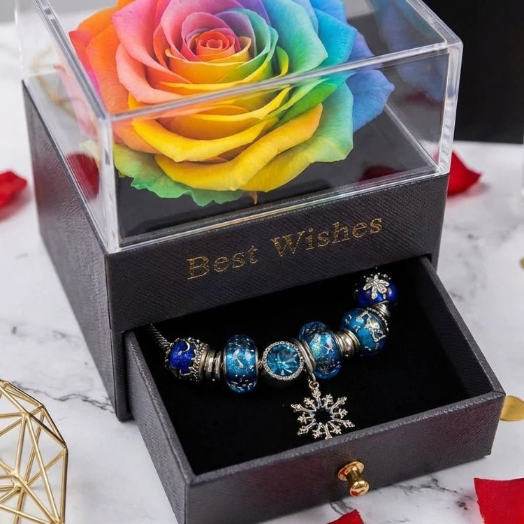 Detailed close-up of a rainbow-colored eternal rose bloom inside a black jewelry box with the drawer pulled open to show a silver bracelet.