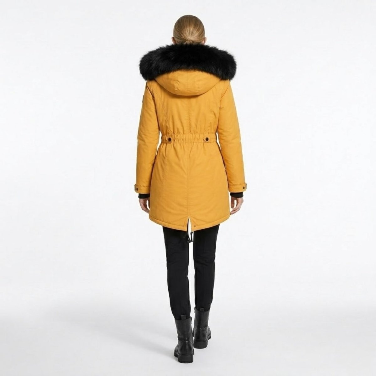 Back view of a female model wearing a Kouvr mustard yellow winter coat showcasing the cinched drawstring waist, fishtail hem, and black faux fur hood detail.