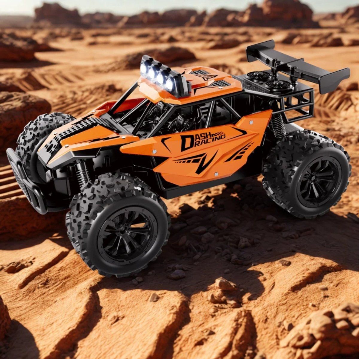 The orange RC racing truck with bright LED headlights on, stationed on rough, rocky desert ground.